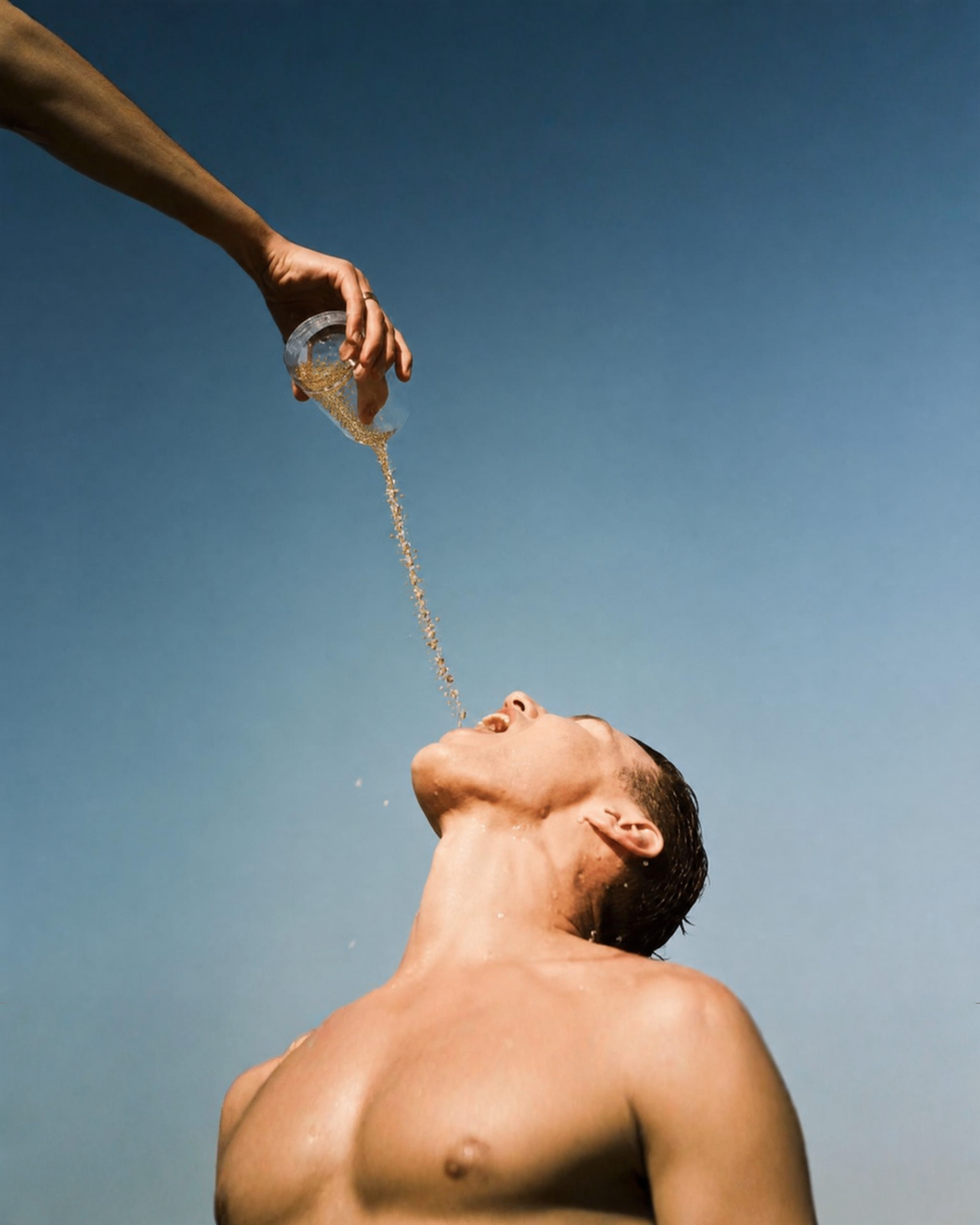 Hand pouring Lova microgranules into a person's mouth against a clear blue sky